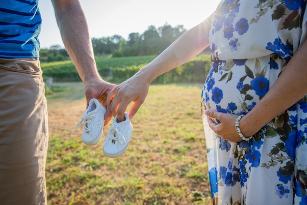 Um casal de pais segura sapatos de bebê a mãe toca sua barriga grávida casal expectante