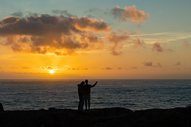 Um casal de pé no penhasco e assistindo o pôr do sol sobre o mar