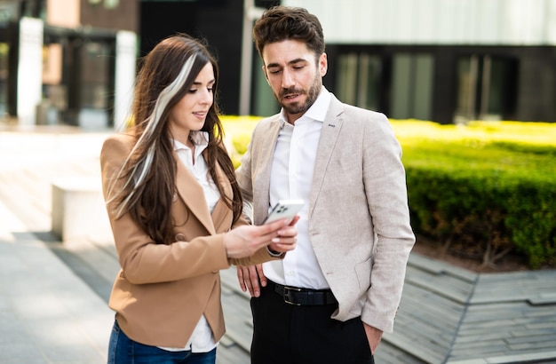 Um casal de pessoas de negócios usando um smartphone ao ar livre