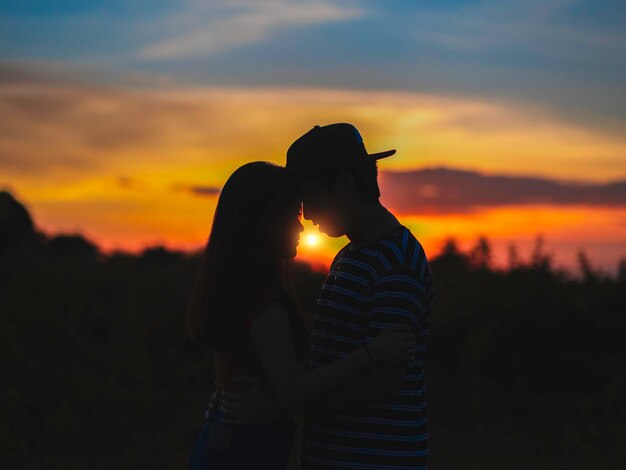 Foto um casal de silhuetas abraçando-se contra o céu laranja durante o pôr do sol