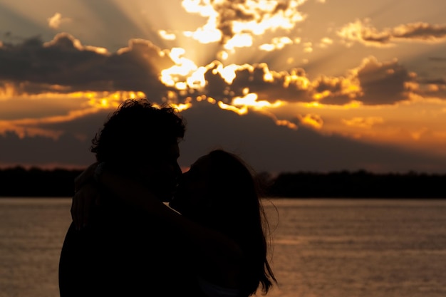 Um casal de siluetas a beijar-se contra o mar ao pôr-do-sol