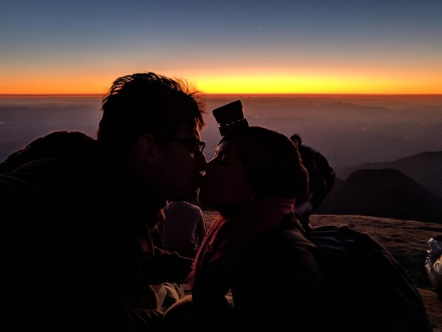 Foto um casal de siluetas a beijar-se na montanha contra o céu durante o pôr-do-sol