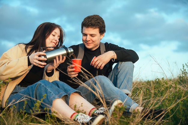 um casal de turistas apaixonados durante a recreação ao ar livre sentam e bebem uma bebida quente de uma garrafa térmica