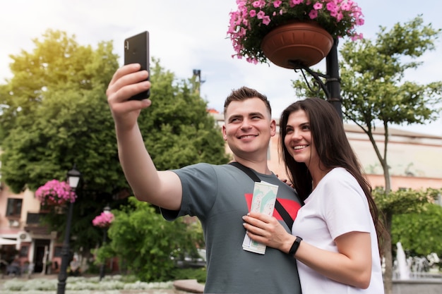 Um casal de turistas apaixonados por um mapa nas mãos, fazendo uma selfie. Namorada e namorado estão olhando para a câmera e sorrindo para uma boa foto. Lindo casal heterossexual está andando na rua.