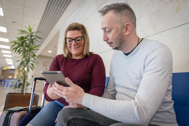 Um casal de turistas usa um tablet enquanto está no aeroporto pronto para viajar