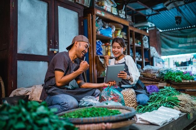 Um casal de vendedores de vegetais sentados e segurando um tablet com gesto de punho