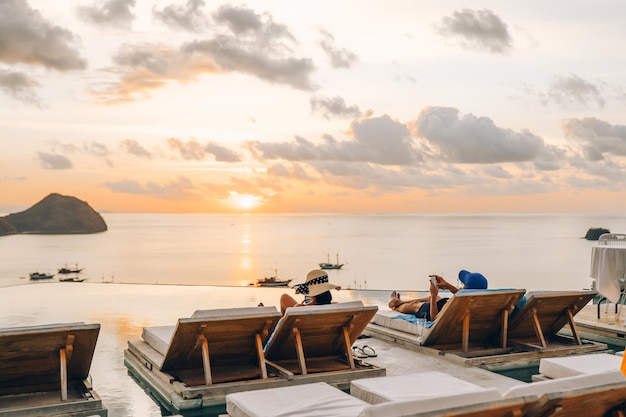 Um casal deitado em uma cadeira relaxante apreciando a vista do pôr do sol e do mar