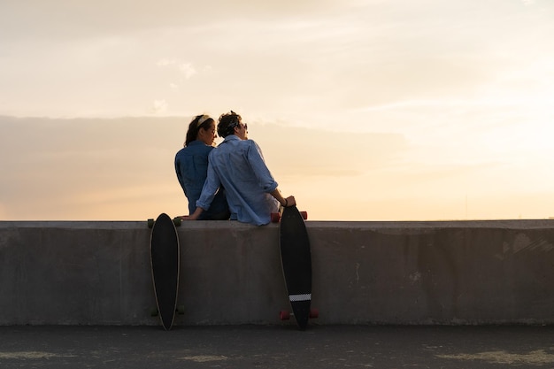 Um casal elegante de longboarders à beira-mar sentado na calçada a ver o pôr-do-sol de verão conceito de estilo de vida