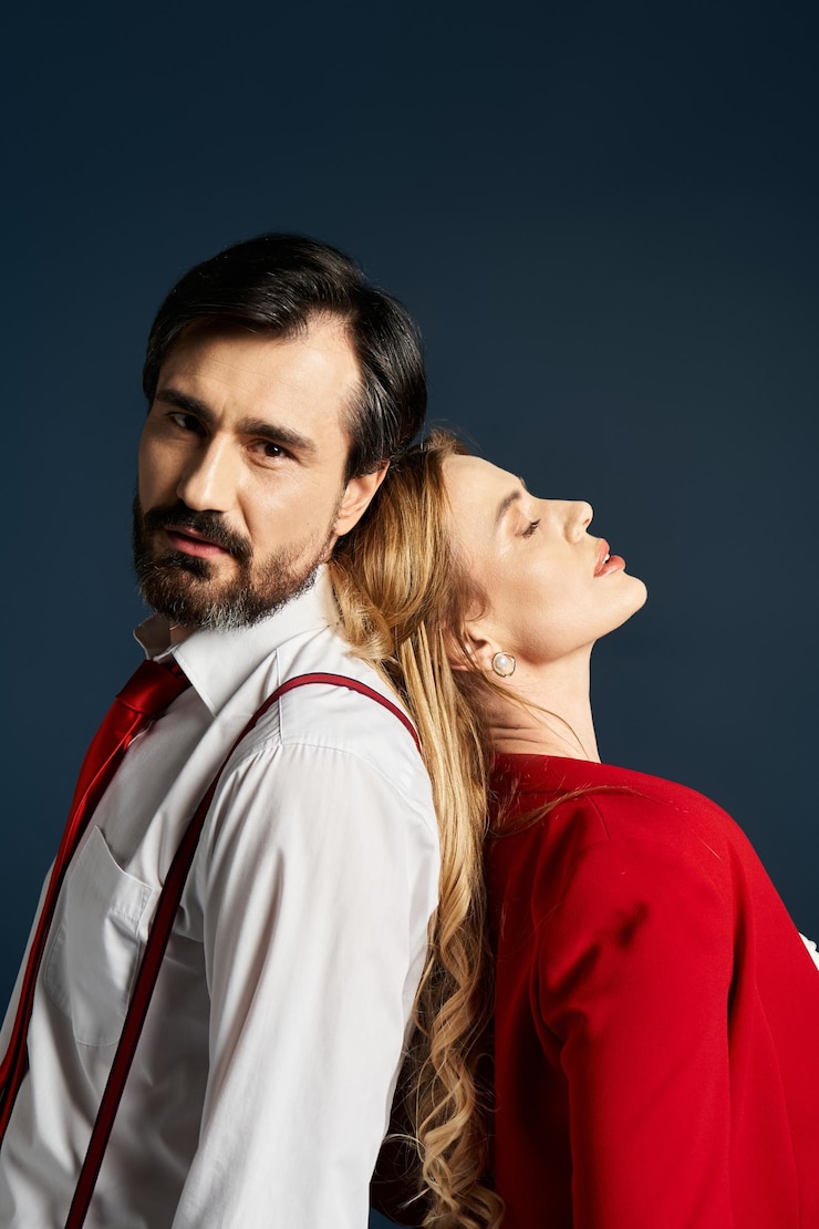 Foto um casal elegante em trajes impressionantes posando contra um fundo azul escuro em um ambiente de estúdio criativo