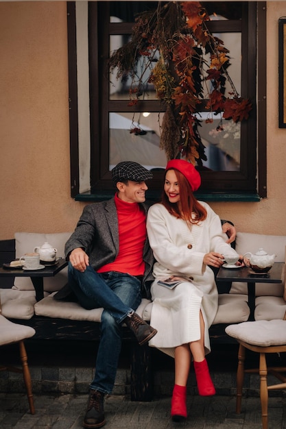Um casal elegante feliz bebe café e sorri enquanto está sentado em um café na rua