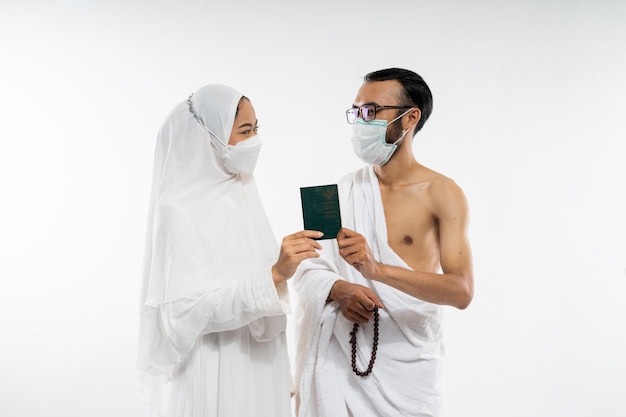 Um casal em roupas ihram e máscara segurando um passaporte juntos quando se olham em b isolado