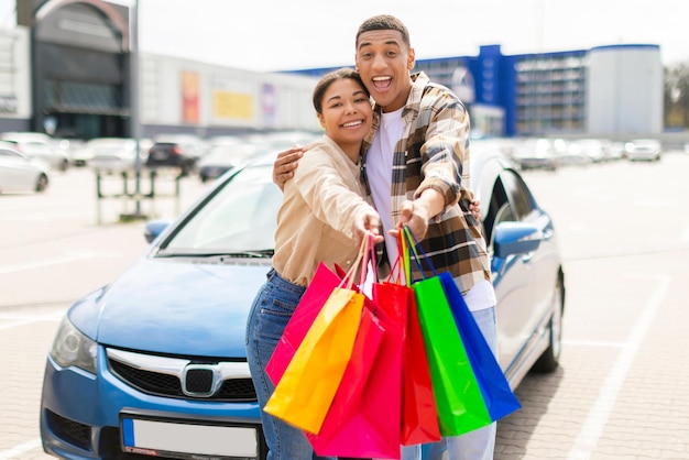 Um casal emocionado de pé junto perto de um carro no estacionamento do centro comercial da cidade segurando sacos de compras