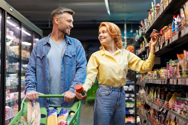 Um casal europeu feliz a fazer compras no supermercado, a escolher e a comprar comida juntos, de pé.