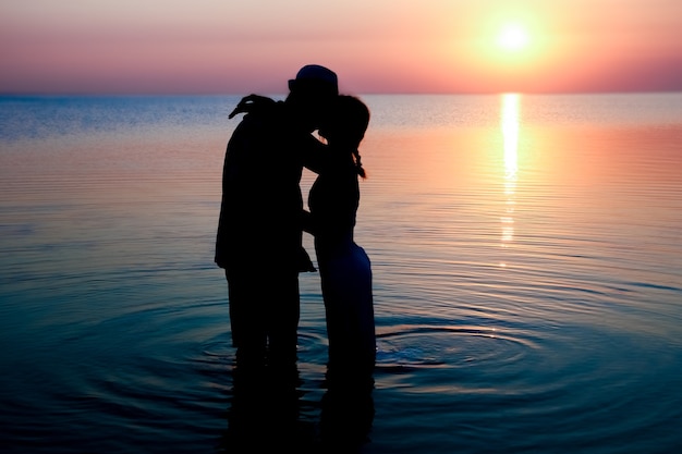 Um casal feliz à beira-mar ao pôr do sol na silhueta de viagens na natureza