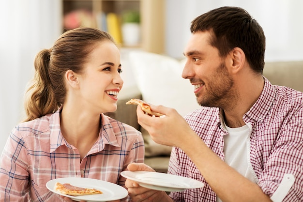 Um casal feliz a comer pizza em casa.