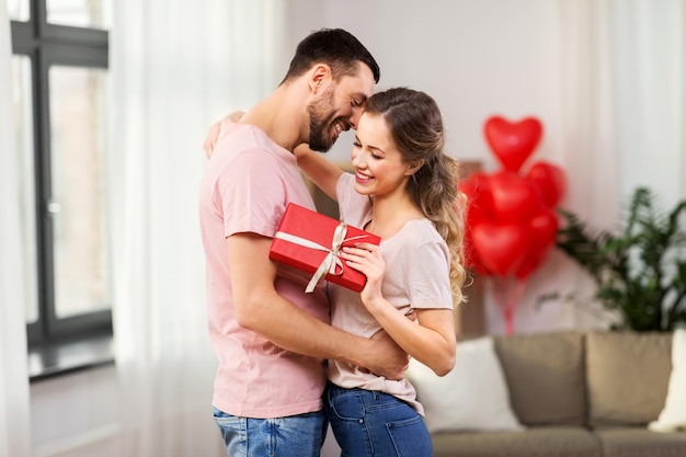 Um casal feliz com uma caixa de presentes a abraçar-se em casa.