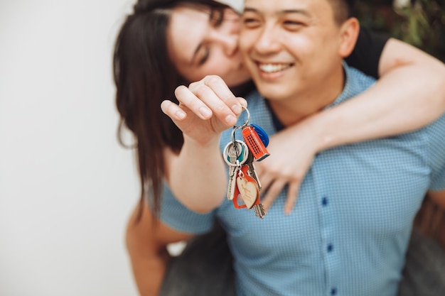 Um casal feliz comemora a mudança para uma nova casa mostra as chaves em um apartamento o conceito de uma hipoteca em imóveis closeup