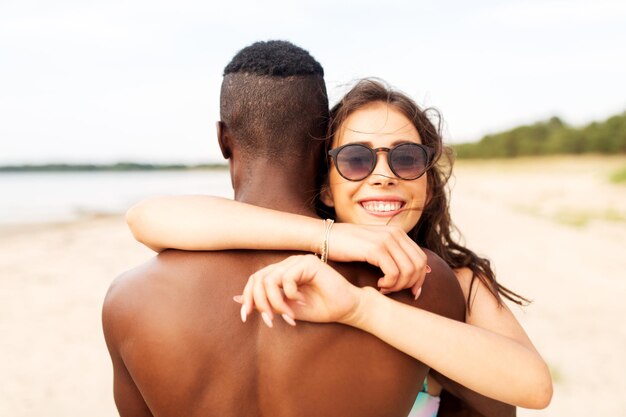 Um casal feliz de raça mista abraçando-se na praia de verão.