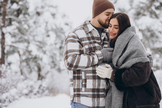 Foto um casal feliz e bonito descansando e bebendo chá quente na floresta no inverno nas montanhas