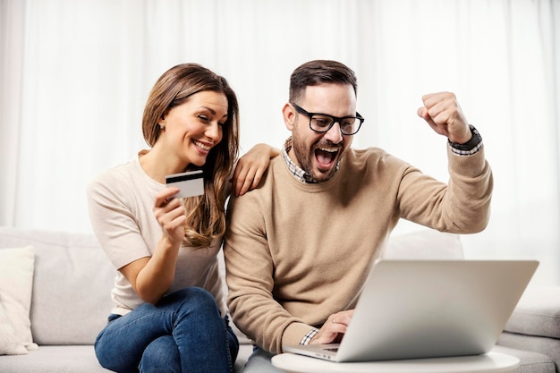 Um casal feliz em sua casa fazendo compras on-line no laptop