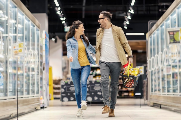 Um casal feliz está pulando e de mãos dadas durante a compra no hipermercado