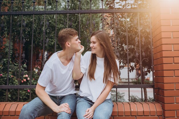 Um casal feliz está sentado em uma cerca de tijolo e rindo.