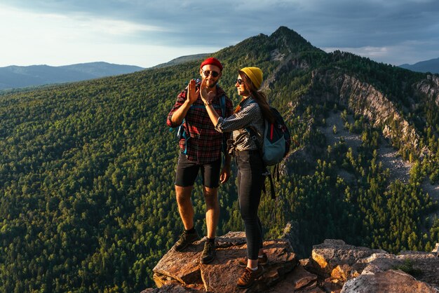 Um casal feliz nas montanhas admira as belas vistas. Um homem e uma mulher com mochilas na montanha admiram a vista panorâmica. Os viajantes gostam de escalar a montanha ao pôr do sol. Copie o espaço