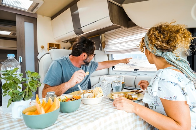 Um casal feliz passando tempo juntos se divertindo durante um almoço vegetariano dentro de uma caravana pessoas olhando pela janela apontando para a vista com o dedo pensando no novo destino