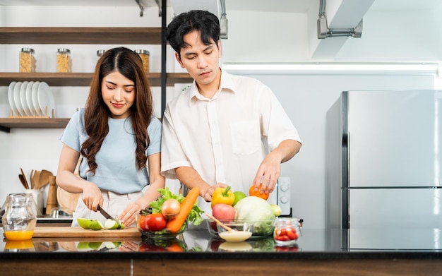 Um casal feliz prepara e cozinha salada saudável com legumes em uma tábua de corte juntos na cozinha de casa Comida para jovem casal marido e mulher de bom humor e relacionamento saudável