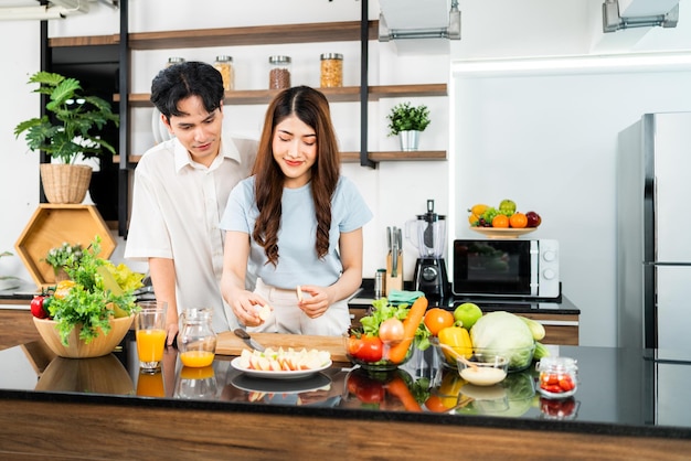 Um casal feliz prepara e cozinha salada saudável com legumes em uma tábua de corte juntos na cozinha de casa Comida para jovem casal marido e mulher de bom humor e relacionamento saudável