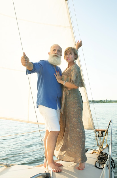 Um casal feliz sênior navegando e sentado ao volante de um barco a vela no lago.