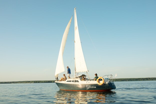 Um casal feliz sênior navegando e sentado ao volante de um barco a vela no lago.