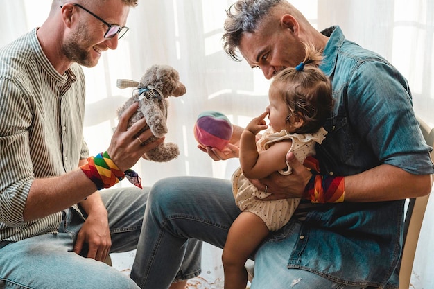 Foto um casal gay a brincar com a filha em casa.