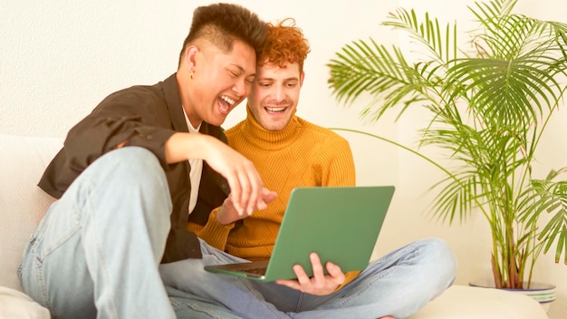 Um casal gay rindo enquanto usa um laptop no sofá