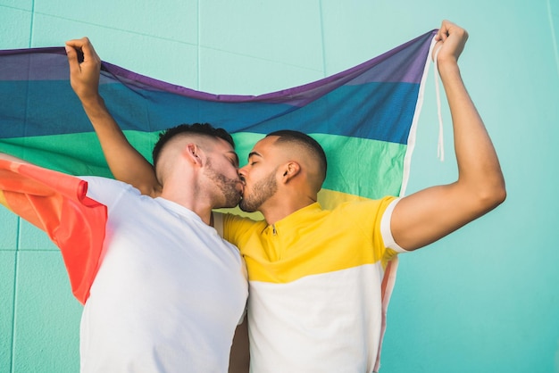 Um casal gay se beijando na boca enquanto segura uma bandeira arco-íris