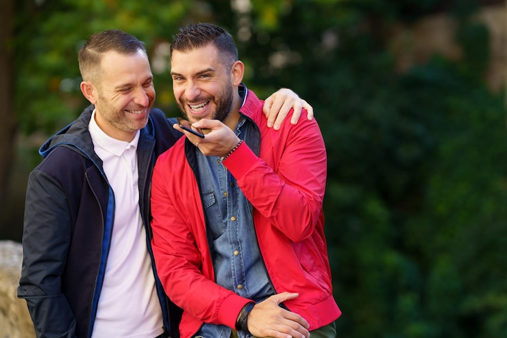 Foto um casal gay sorridente a falar por telemóvel.
