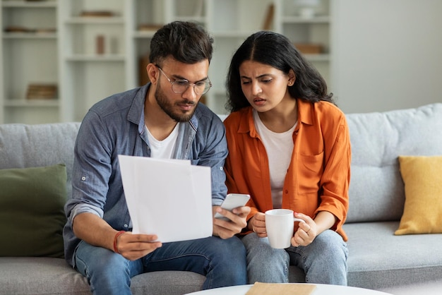 Um casal indiano lê papéis e calcula gastos planejando o orçamento juntos usando o celular