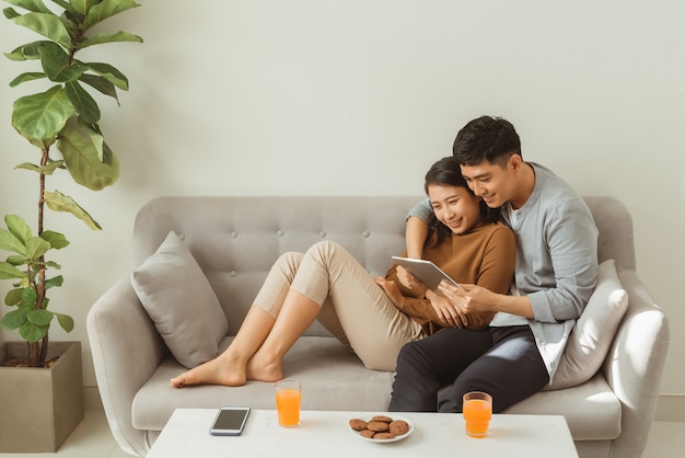 Um casal jovem e atraente está sentado em um sofá e está lendo um tablet juntos.