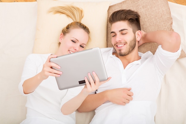 Um casal jovem e feliz com um tablet Pc na cama de cima.