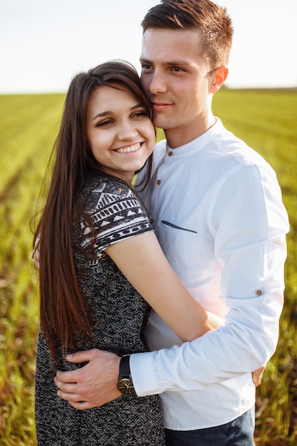 Um casal jovem, feliz e amoroso, de pé em um campo verde, contra o céu pelas mãos e se divertindo