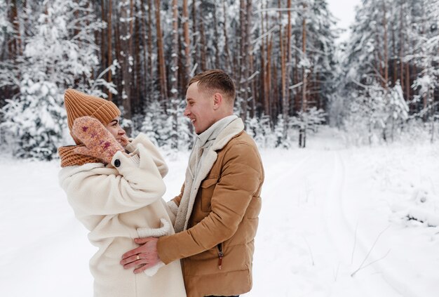 Um casal jovem, feliz e amoroso se abraça em uma floresta coberta de neve.