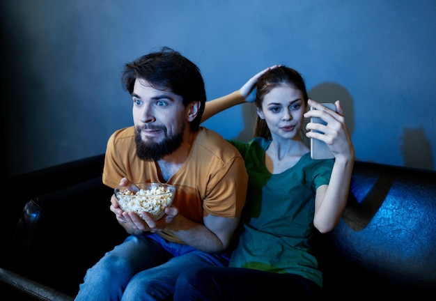 Um casal no sofá assistindo tv e pipoca dentro de casa