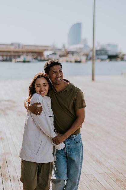 Um casal radiante abraça-se num calçadão ensolarado de Barcelona, exalando felicidade e amor.