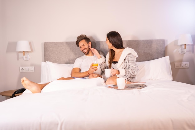 Um casal recém-acordado de pijama tomando café e suco de laranja no café da manhã