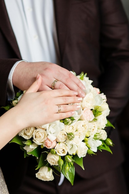 Um casal recém-casado coloca as mãos em um buquê de casamento mostrando seus anéis de casamento