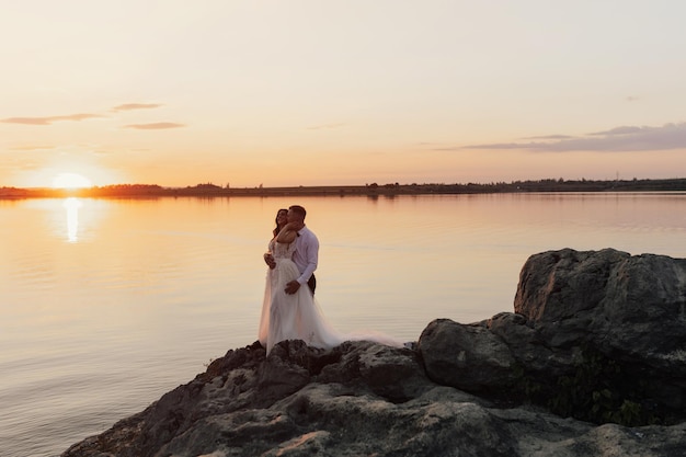 Um casal se abraça na margem de um lago ao pôr do sol.
