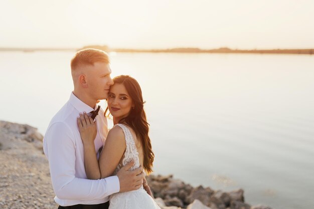 Um casal se abraça na praia em frente a um lago.