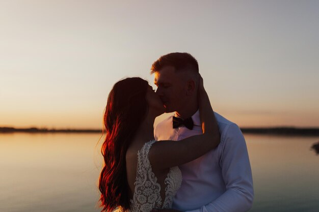 Um casal se beijando em frente a um lago ao pôr do sol