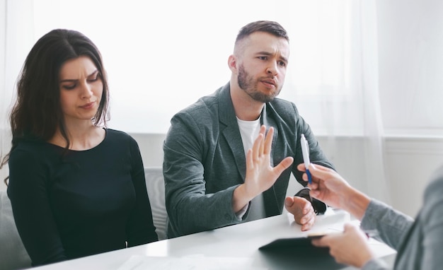 Um casal senta-se em uma mesa em uma reunião com um advogado com o homem fazendo gestos e se recusando a assinar