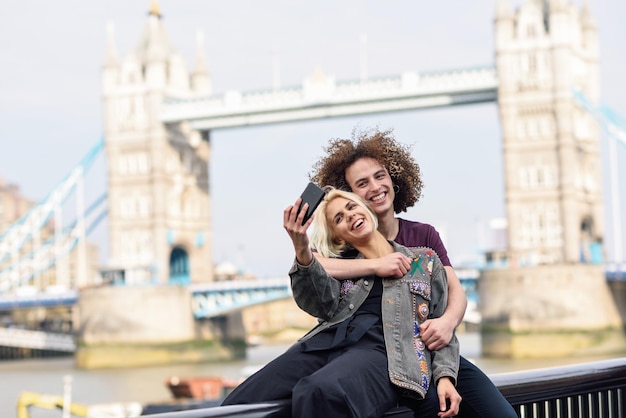 Foto um casal sorridente a tirar uma selfie na cidade.